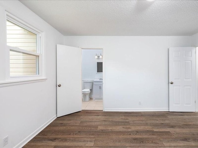 unfurnished bedroom featuring a textured ceiling, ensuite bathroom, and dark wood-type flooring