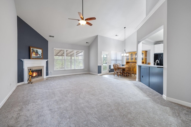 unfurnished living room featuring ceiling fan with notable chandelier, light carpet, and high vaulted ceiling