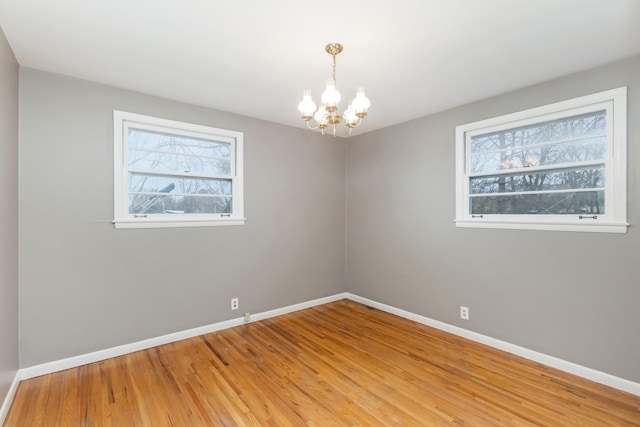 empty room with plenty of natural light, a chandelier, and hardwood / wood-style flooring