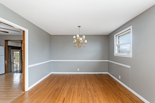 spare room featuring wood-type flooring, an inviting chandelier, and a healthy amount of sunlight