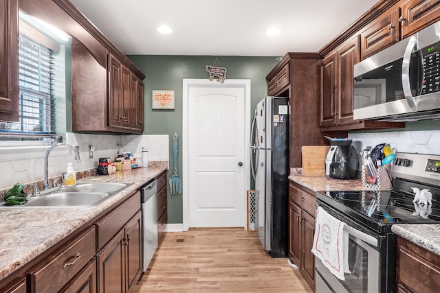 kitchen featuring sink, stainless steel appliances, light stone counters, light hardwood / wood-style flooring, and decorative backsplash