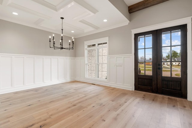 unfurnished dining area featuring an inviting chandelier, french doors, light wood-type flooring, ornamental molding, and beam ceiling