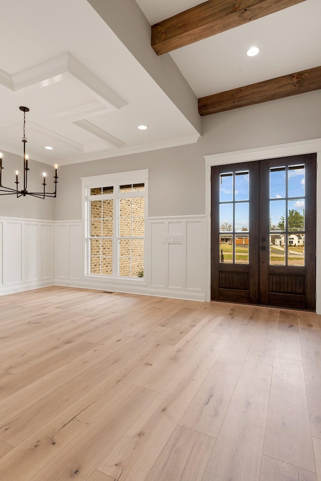 unfurnished living room with beamed ceiling, a notable chandelier, light hardwood / wood-style floors, and french doors