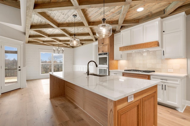 kitchen with light stone counters, sink, a large island with sink, decorative light fixtures, and white cabinetry