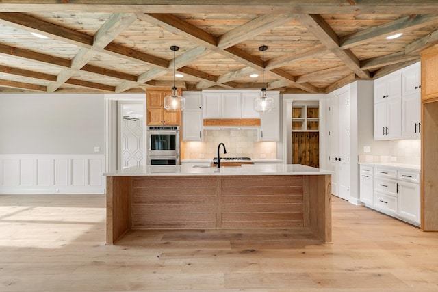 kitchen featuring white cabinets, a center island with sink, light hardwood / wood-style flooring, and hanging light fixtures