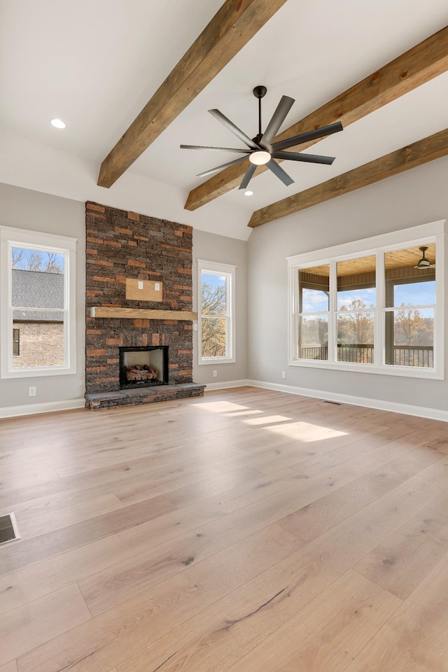 unfurnished living room featuring beam ceiling, a wealth of natural light, a fireplace, and light wood-type flooring