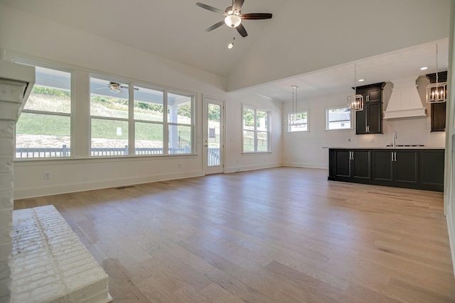 unfurnished living room with light wood-type flooring, high vaulted ceiling, plenty of natural light, and sink