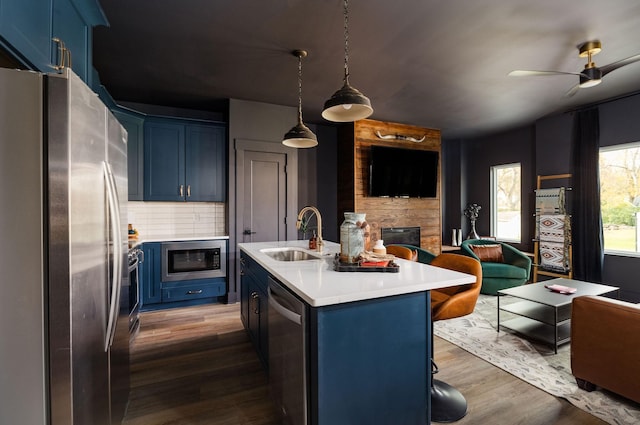 kitchen featuring blue cabinetry, sink, stainless steel appliances, an island with sink, and decorative backsplash