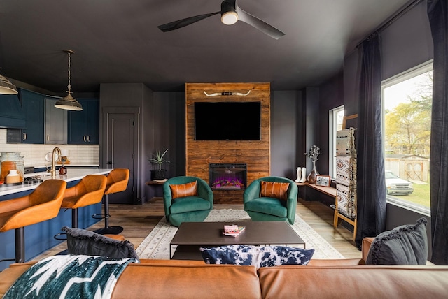 living room featuring light hardwood / wood-style flooring, ceiling fan, a stone fireplace, and sink