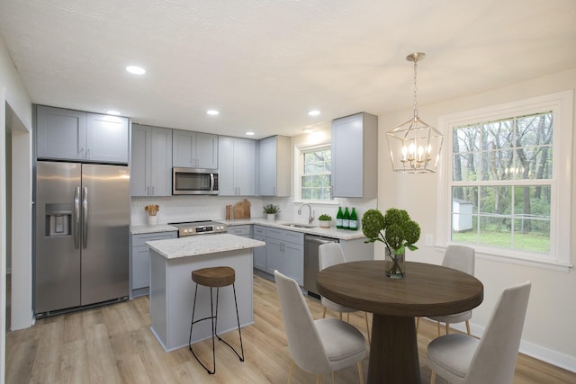 kitchen featuring sink, stainless steel appliances, light hardwood / wood-style flooring, pendant lighting, and a kitchen island