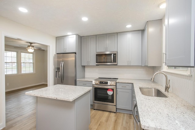 kitchen with light stone countertops, a center island, sink, stainless steel appliances, and light hardwood / wood-style flooring