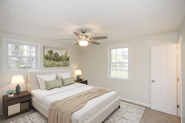 bedroom with a textured ceiling, light colored carpet, multiple windows, and ceiling fan