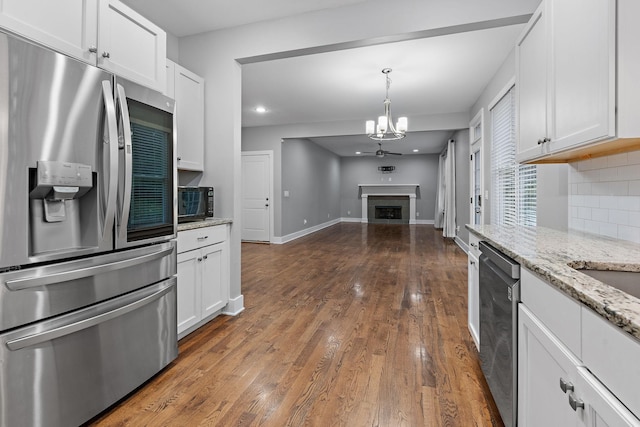 kitchen with light stone countertops, appliances with stainless steel finishes, dark wood-type flooring, white cabinets, and a chandelier