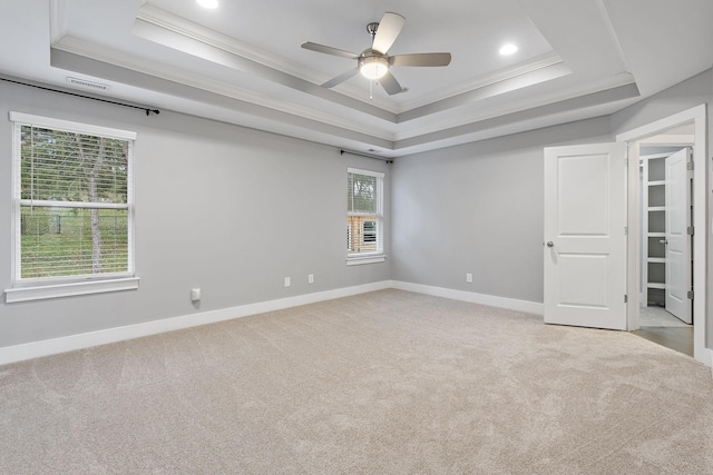 empty room with a raised ceiling, ceiling fan, light colored carpet, and ornamental molding