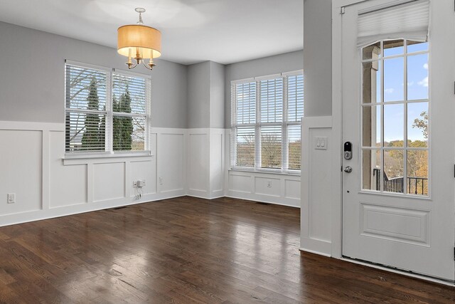 unfurnished dining area featuring a notable chandelier, dark hardwood / wood-style floors, and a healthy amount of sunlight