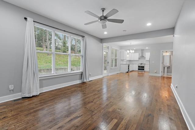 unfurnished living room featuring ceiling fan with notable chandelier and dark wood-type flooring