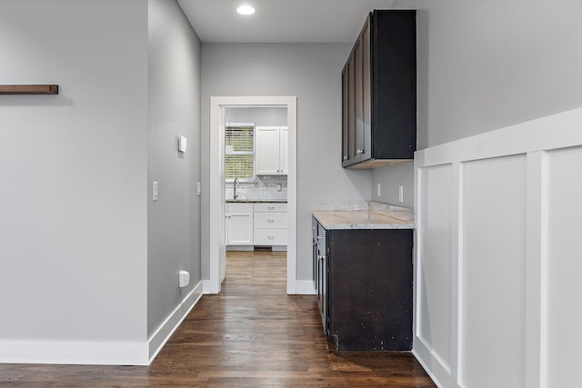 interior space with dark hardwood / wood-style flooring, light stone counters, dark brown cabinets, sink, and white cabinets