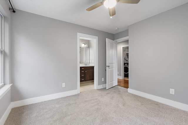 unfurnished bedroom featuring sink, ensuite bath, ceiling fan, light colored carpet, and washer / dryer