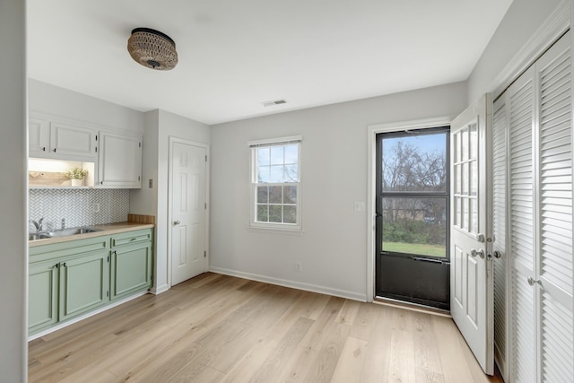 kitchen with light wood-type flooring, backsplash, sink, green cabinetry, and white cabinetry