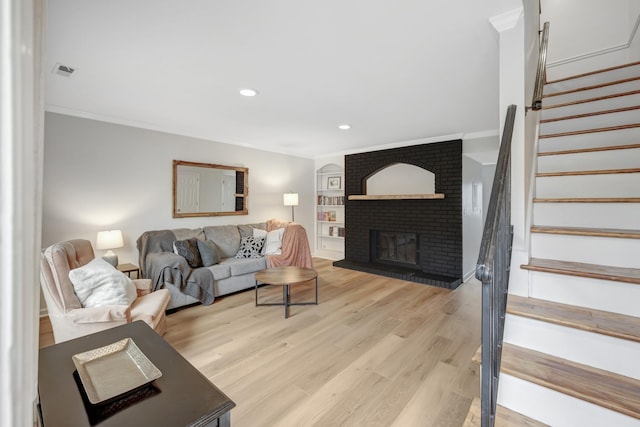 living room featuring light wood-type flooring, a brick fireplace, and ornamental molding