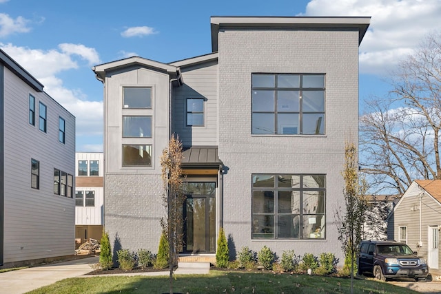 modern home featuring a standing seam roof, metal roof, and brick siding