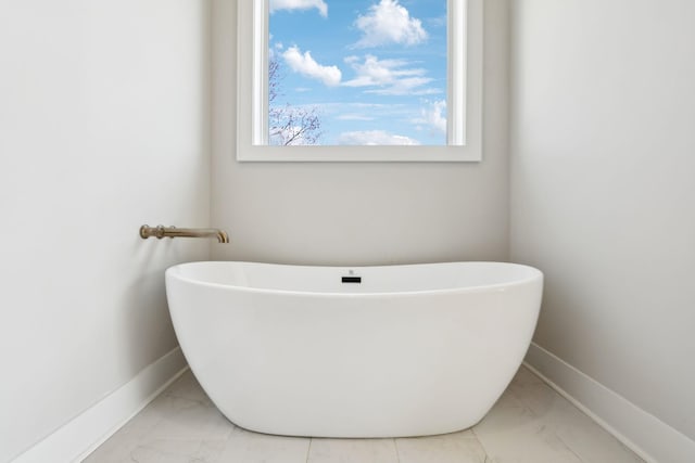 full bath with marble finish floor, baseboards, and a freestanding bath