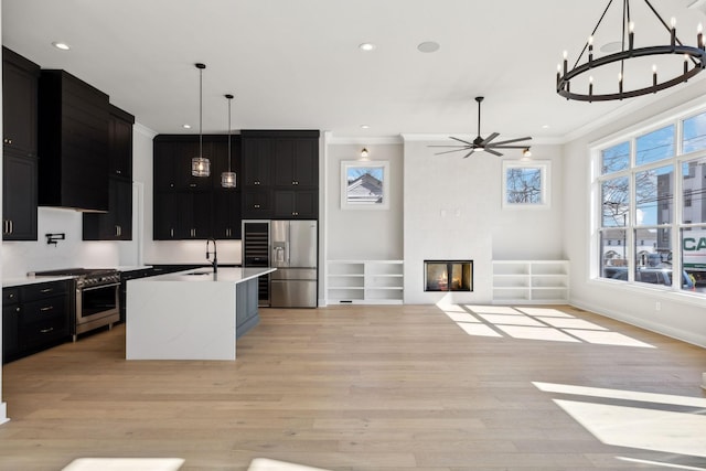 kitchen featuring stainless steel appliances, light wood-style flooring, ornamental molding, a large fireplace, and dark cabinets