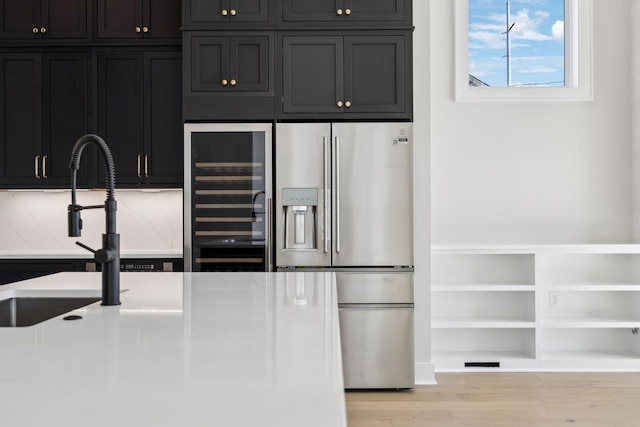 kitchen featuring a sink, wood finished floors, dark cabinets, beverage cooler, and stainless steel fridge