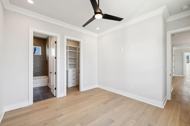 unfurnished bedroom with recessed lighting, baseboards, ornamental molding, light wood finished floors, and a walk in closet