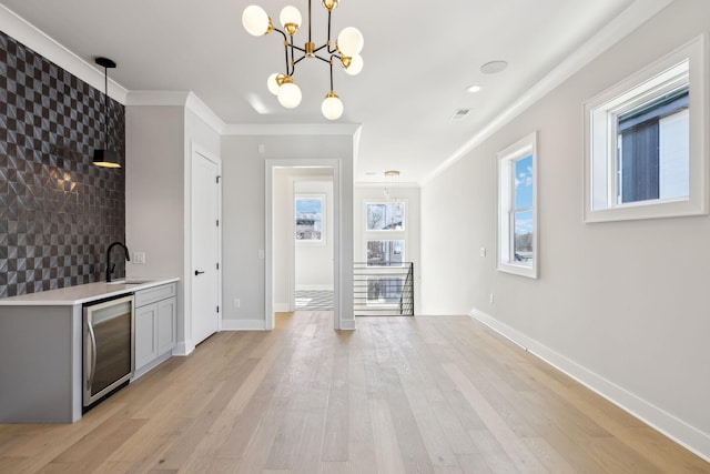 bar with wine cooler, crown molding, hanging light fixtures, a sink, and light wood-type flooring