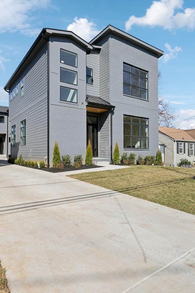 modern home with a standing seam roof, concrete driveway, and a front yard