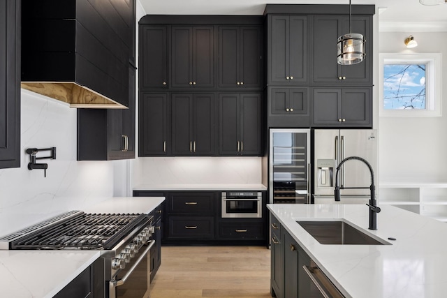 kitchen with stainless steel appliances, a sink, light stone countertops, dark cabinets, and light wood-type flooring