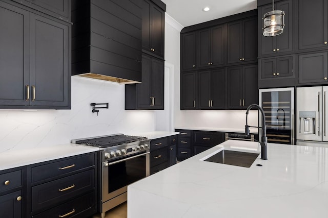 kitchen with appliances with stainless steel finishes, light stone counters, dark cabinets, wall chimney range hood, and a sink