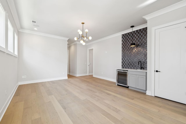 unfurnished living room with a chandelier, beverage cooler, baseboards, light wood-type flooring, and crown molding