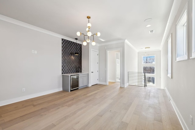 unfurnished living room with a notable chandelier, visible vents, light wood-style flooring, ornamental molding, and beverage cooler