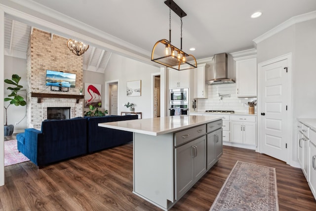 kitchen featuring dark wood-type flooring, hanging light fixtures, a brick fireplace, wall chimney exhaust hood, and appliances with stainless steel finishes