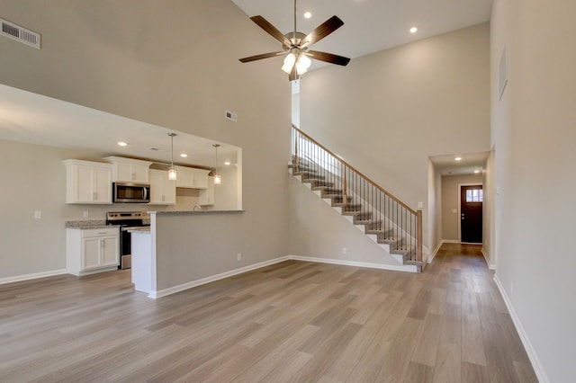 unfurnished living room featuring a high ceiling, light wood-type flooring, and ceiling fan