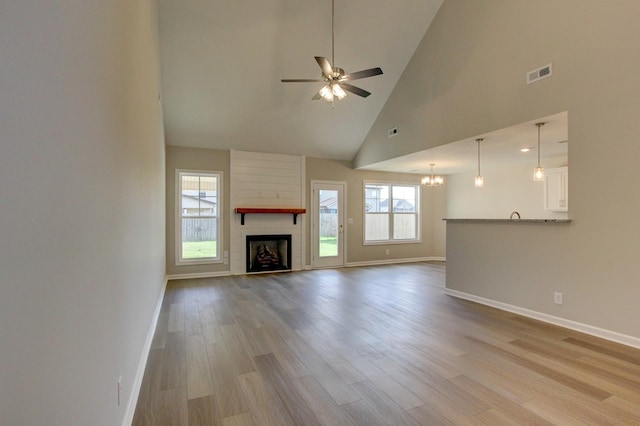 unfurnished living room with ceiling fan with notable chandelier, a large fireplace, light hardwood / wood-style flooring, and high vaulted ceiling