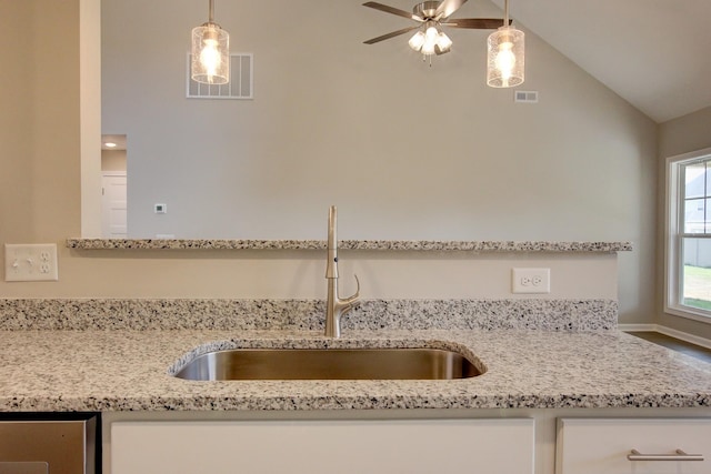 kitchen with light stone counters, sink, decorative light fixtures, and vaulted ceiling