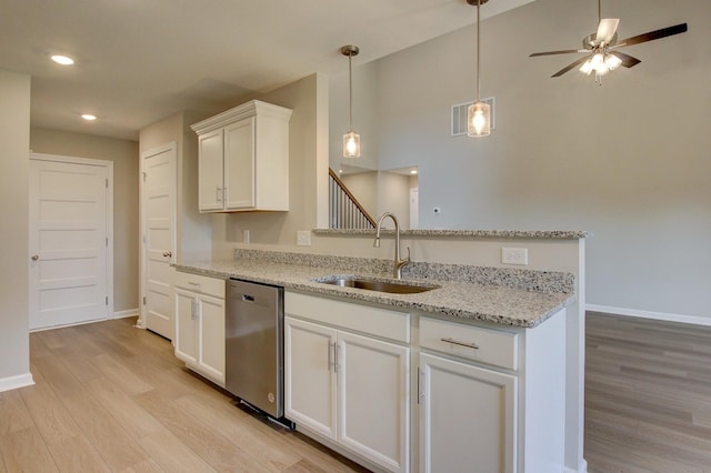 kitchen with sink, light hardwood / wood-style flooring, stainless steel dishwasher, light stone counters, and white cabinetry