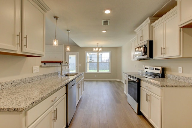 kitchen with light stone counters, stainless steel appliances, sink, pendant lighting, and light hardwood / wood-style flooring