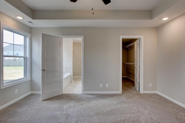 unfurnished bedroom featuring ensuite bath, a spacious closet, ceiling fan, light colored carpet, and a closet