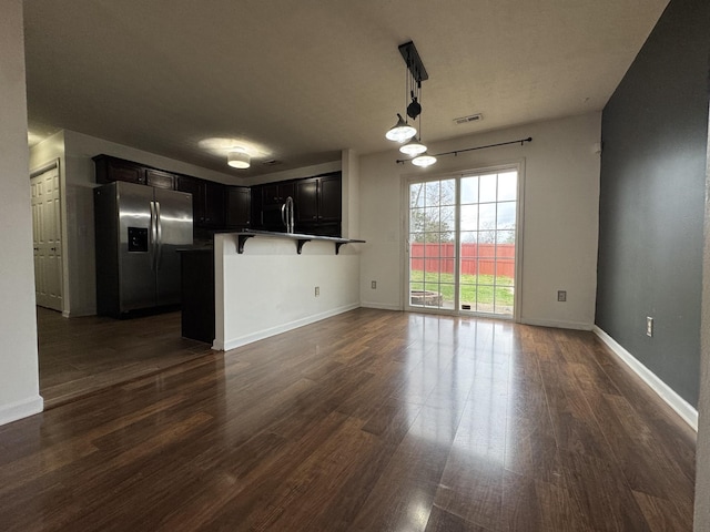 kitchen featuring dark wood-type flooring, a kitchen breakfast bar, stainless steel refrigerator with ice dispenser, hanging light fixtures, and kitchen peninsula