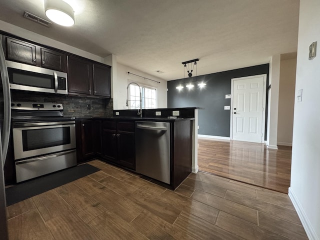 kitchen with dark hardwood / wood-style floors, appliances with stainless steel finishes, tasteful backsplash, decorative light fixtures, and kitchen peninsula