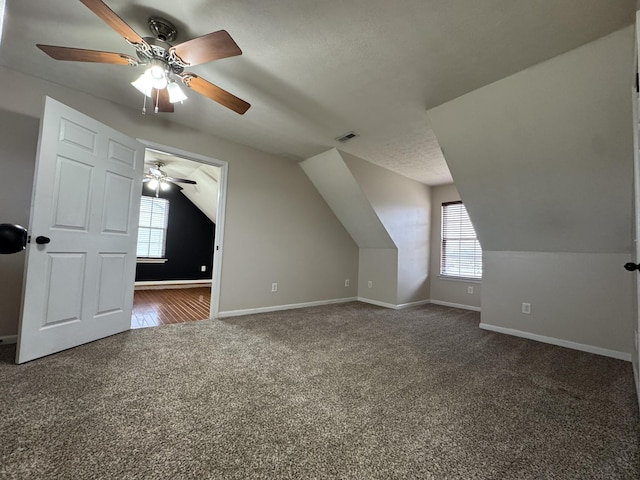 bonus room with a textured ceiling, ceiling fan, dark carpet, and vaulted ceiling