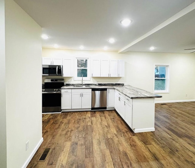 kitchen with white cabinets, kitchen peninsula, dark wood-type flooring, and appliances with stainless steel finishes