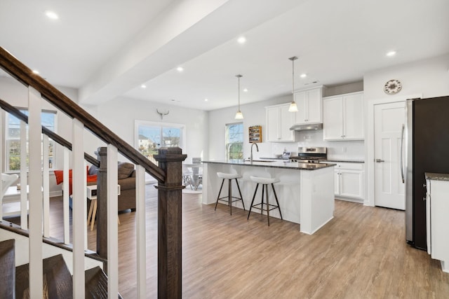 kitchen with a wealth of natural light, white cabinets, stainless steel appliances, and an island with sink