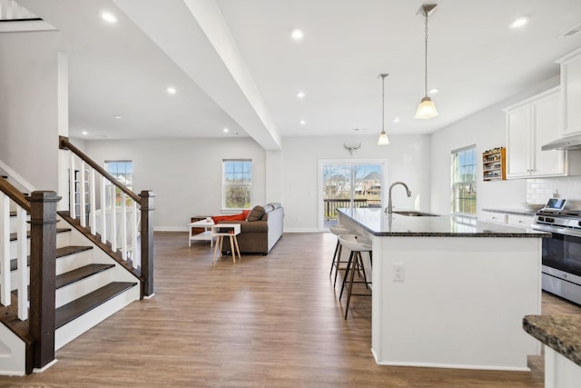 kitchen with stainless steel range, an island with sink, wood-type flooring, and sink