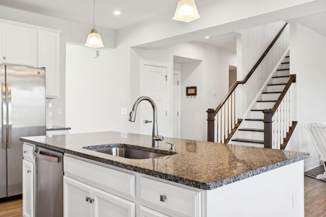 kitchen with a kitchen island with sink, white cabinets, sink, light wood-type flooring, and stainless steel appliances