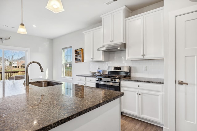 kitchen with dark stone countertops, stainless steel gas stove, white cabinets, and sink